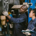 Auto garage worker Black African working together to fix service car vahicle wheel support together