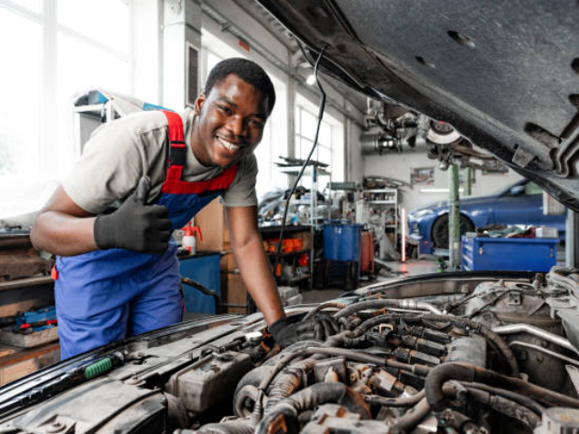 Young African auto mechanic checking car engine under the hood in auto service close up